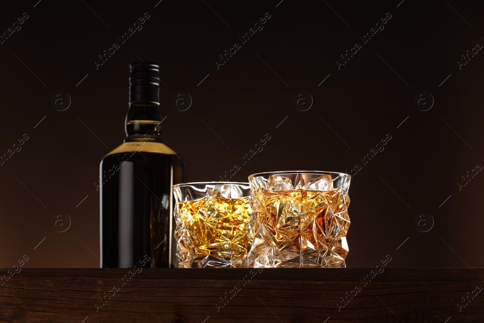 Photo of Whiskey with ice cubes in glasses and bottle on wooden table, low angle view