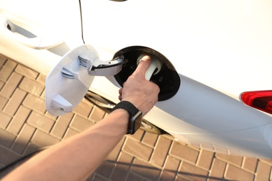 Photo of Man inserting plug into electric car socket at charging station, above view