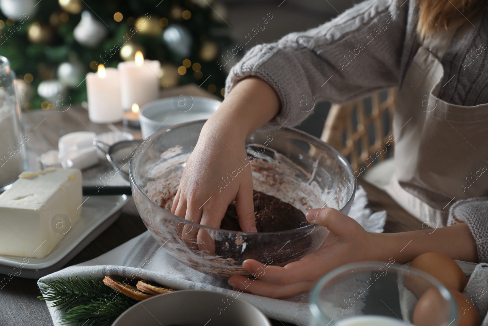 Photo of Little child making Christmas pastry at wooden table, closeup