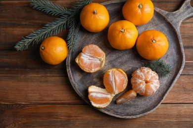 Photo of Tray with delicious ripe tangerines and fir branches on wooden table, flat lay