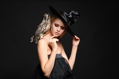 Photo of Witch in black hat with owl on dark background. Scary fantasy character
