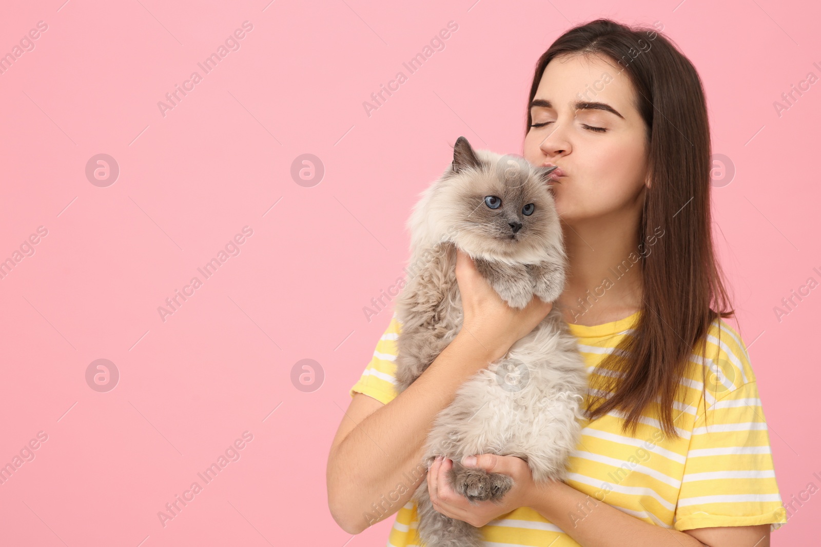 Photo of Woman kissing her cute cat on pink background, space for text