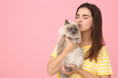 Photo of Woman kissing her cute cat on pink background, space for text