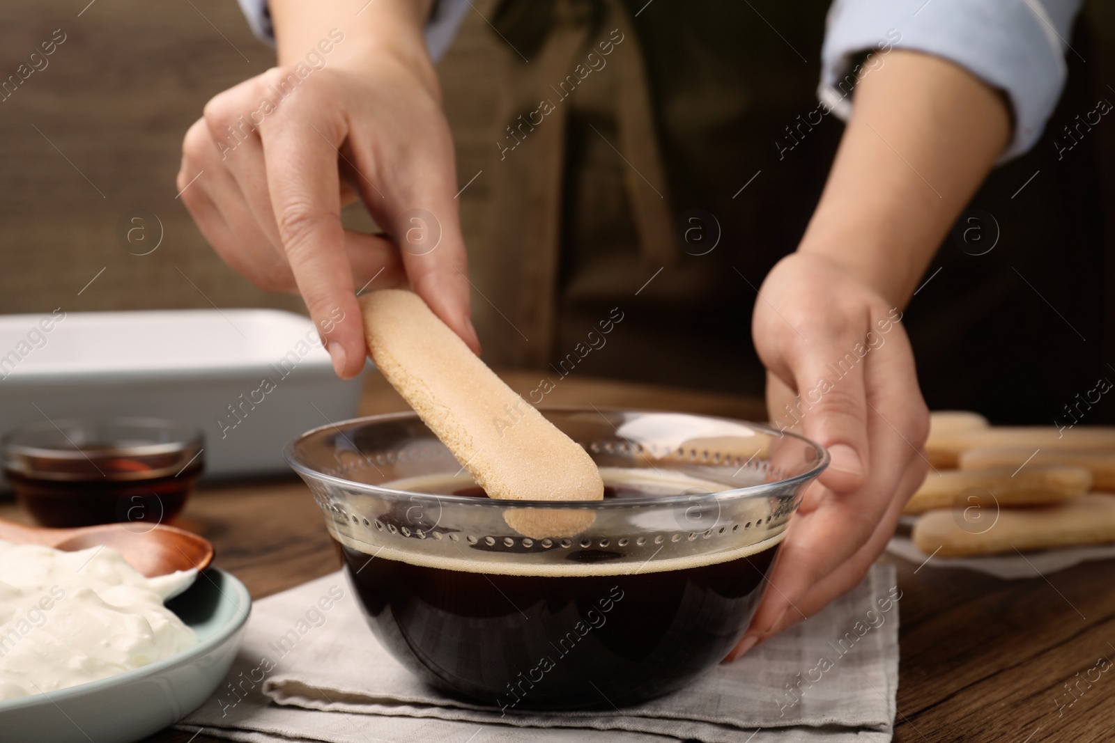 Photo of Woman making tiramisu cake at wooden table, closeup