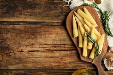 Photo of Fresh baby corn cobs on wooden table, flat lay. Space for text