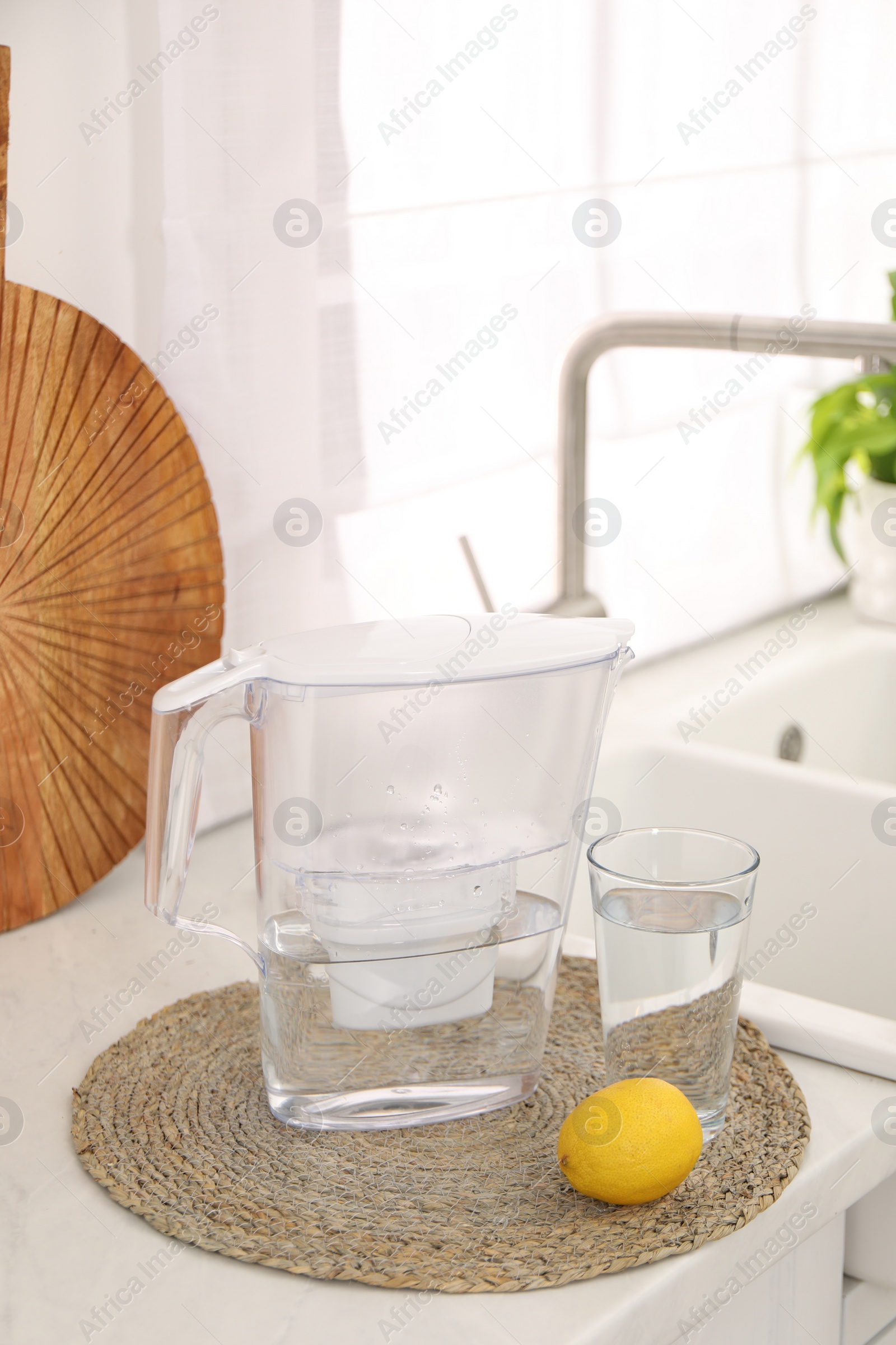 Photo of Water filter jug, glass and lemon on countertop in kitchen