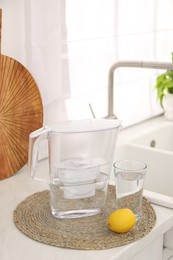 Photo of Water filter jug, glass and lemon on countertop in kitchen