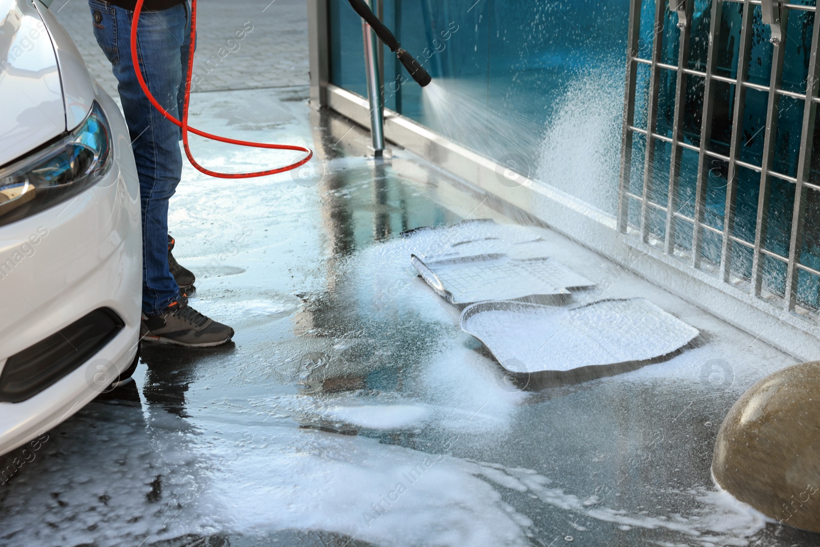 Photo of Man cleaning auto mats with high pressure foam jet at self-service car wash, closeup