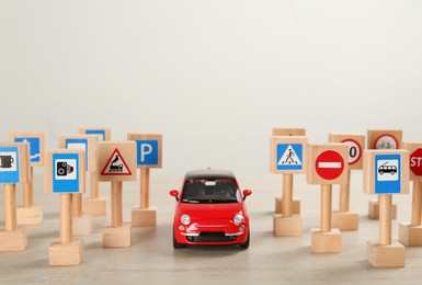 Photo of Many different miniature road signs and car on wooden table, space for text. Driving school