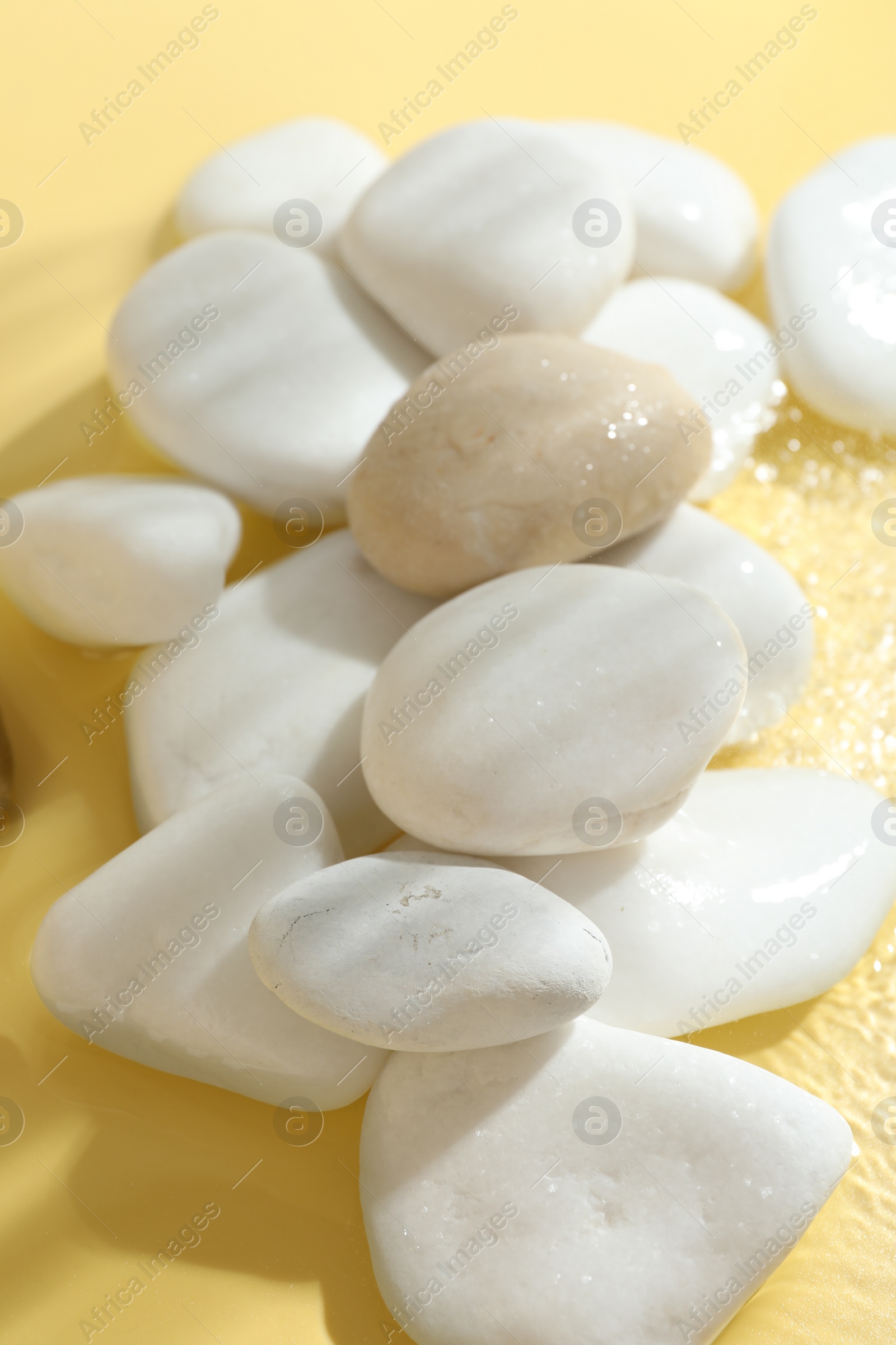 Photo of Spa stones in water on yellow background, closeup