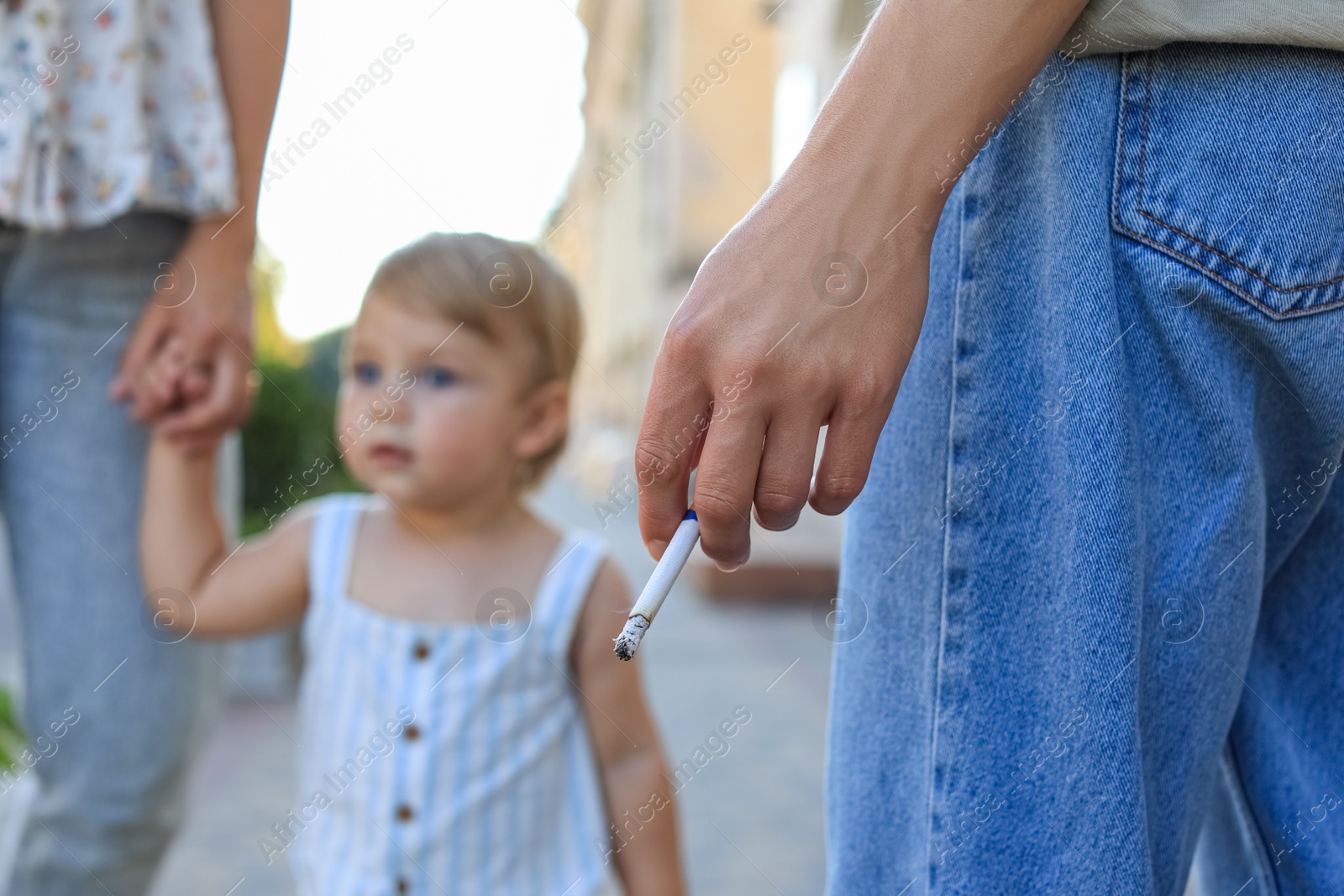 Photo of Woman smoking cigarette in public place outdoors, closeup. Don't smoke near kids