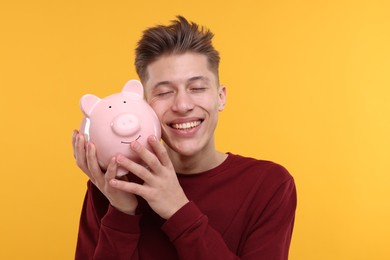 Photo of Happy man with piggy bank on yellow background