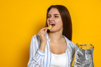 Photo of Pretty young woman eating tasty potato chips on yellow background