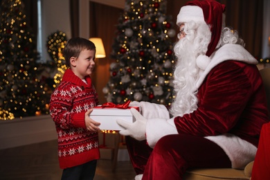 Santa Claus giving present to little boy in room decorated for Christmas