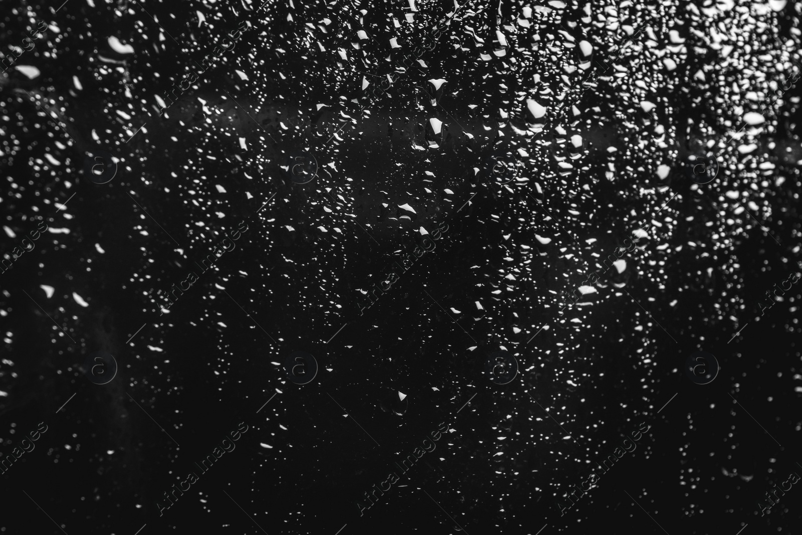 Photo of Glass with rain drops on black background