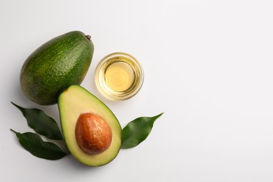 Photo of Cooking oil in bowl and fresh avocados on white background, flat lay. Space for text