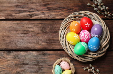 Photo of Colorful Easter eggs in decorative nest and willow branches on wooden background, flat lay. Space for text