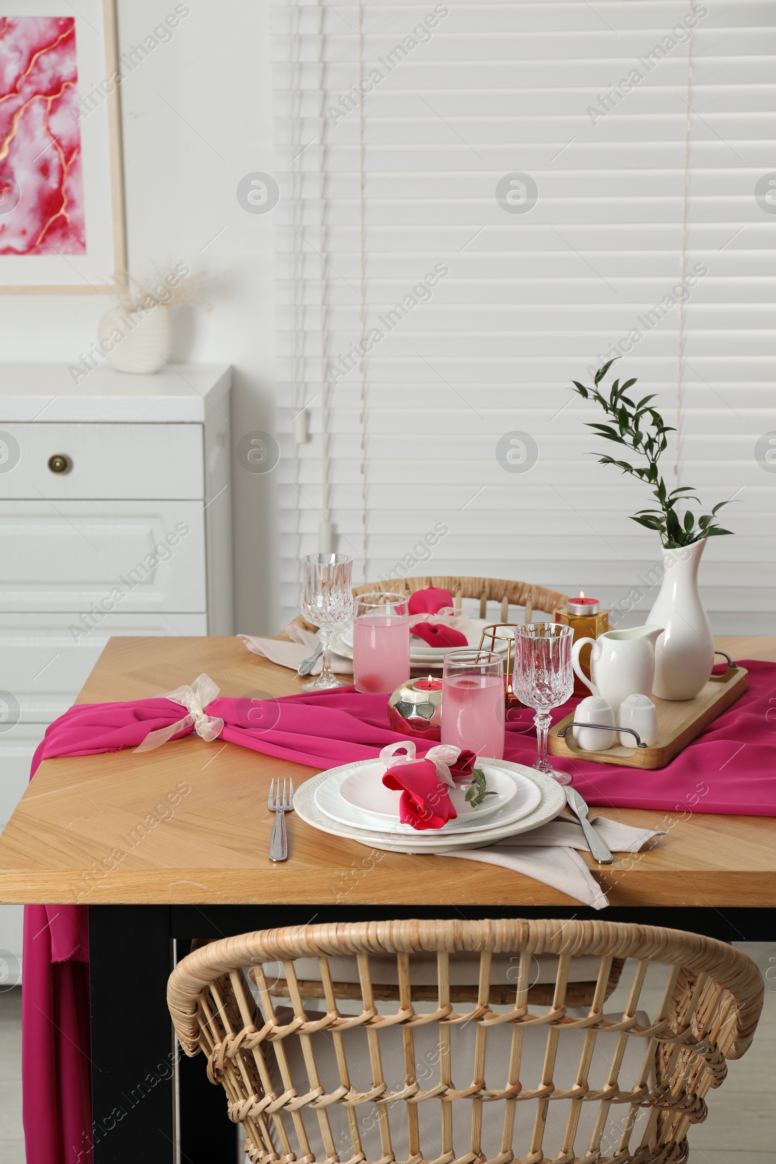 Photo of Color accent table setting. Glasses, plates, pink napkins and vase with green branch in dining room