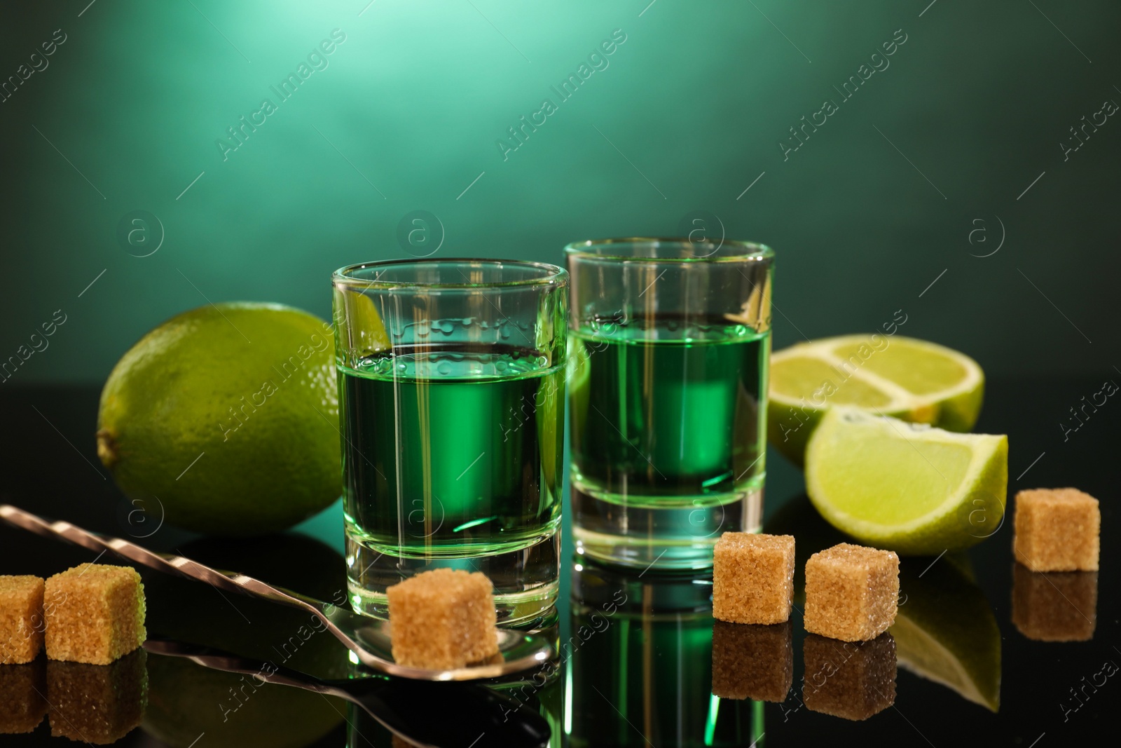 Photo of Absinthe in shot glasses, brown sugar, lime and spoon on mirror table. Alcoholic drink