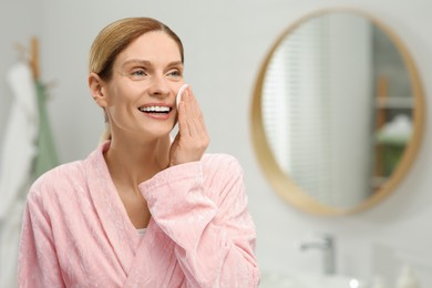 Beautiful woman removing makeup with cotton pad indoors, space for text