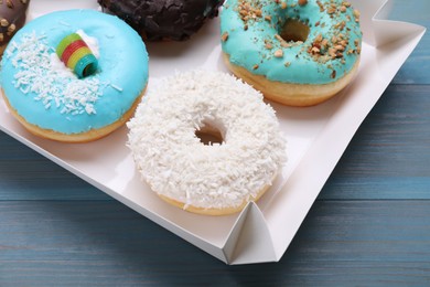 Photo of Box with different tasty glazed donuts on light blue wooden table, closeup