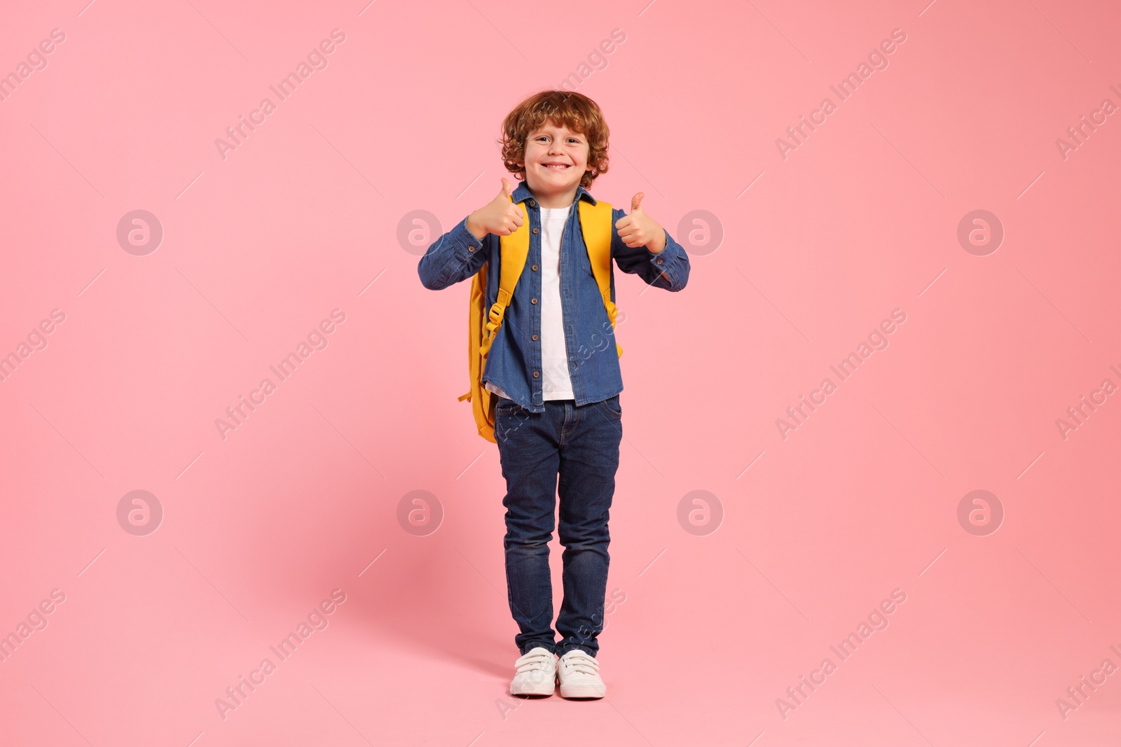 Photo of Happy schoolboy with backpack showing thumbs up gesture on pink background