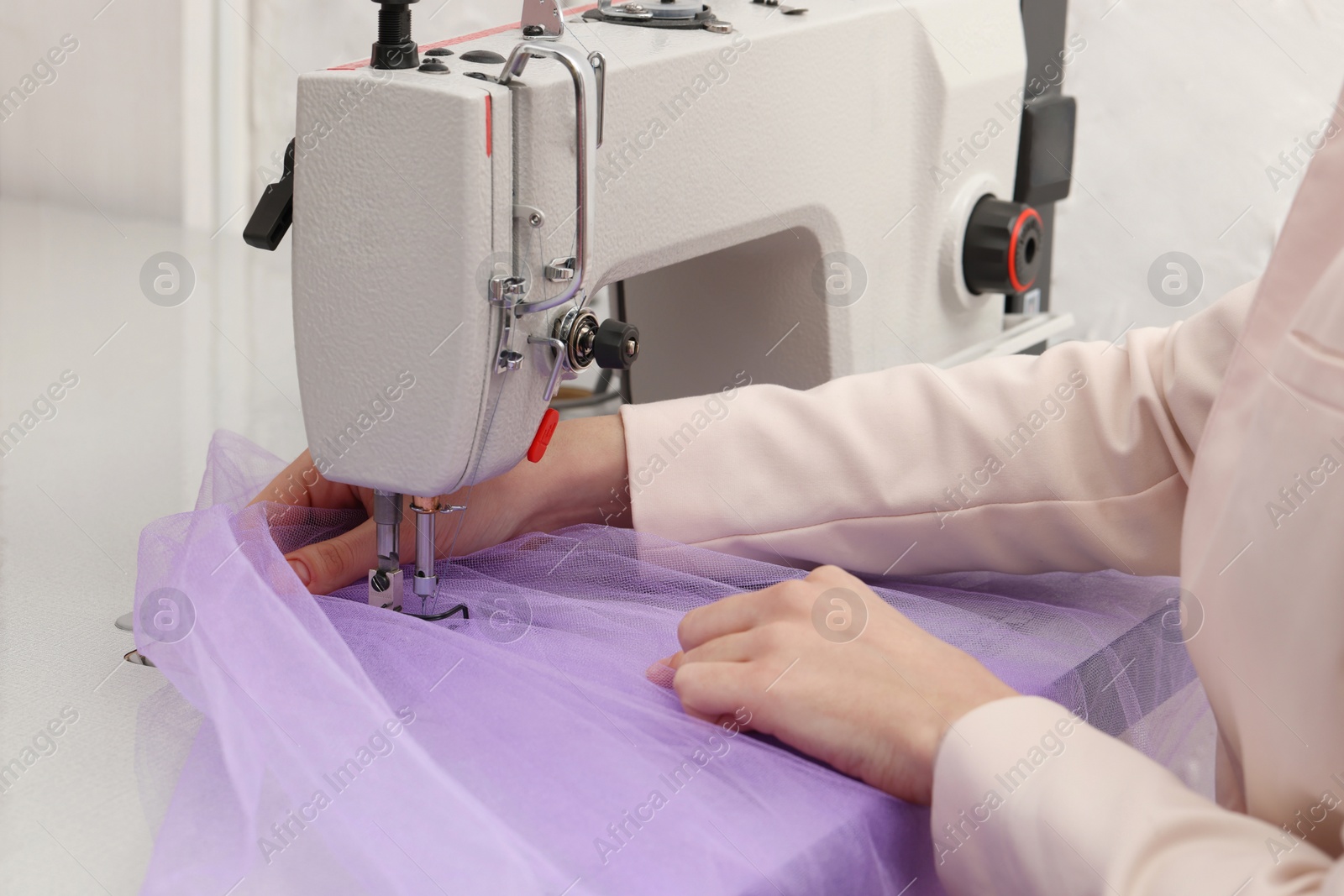 Photo of Dressmaker sewing new dress with machine in atelier, closeup