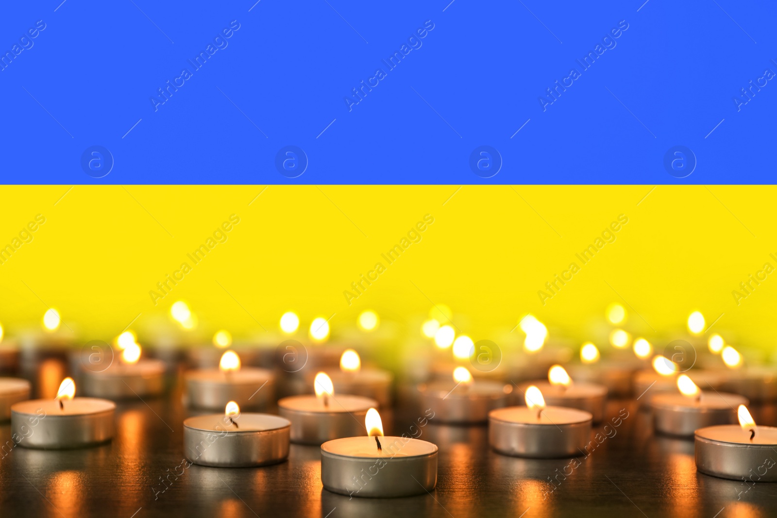 Image of Many burning candles and Ukrainian national flag on background