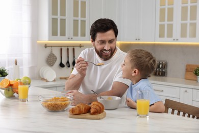 Photo of Father and his cute little son having breakfast at table in kitchen