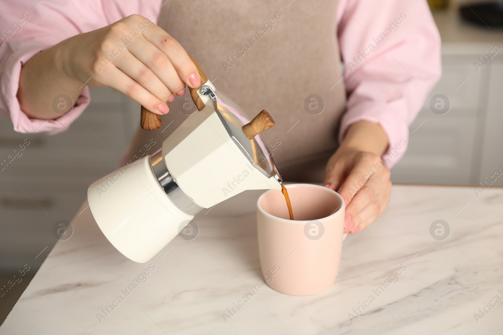 Photo of Woman pouring aromatic coffee from moka pot into cup at white marble table, closeup