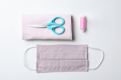 Homemade protective mask and sewing accessories on white background, flat lay