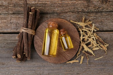 Dried sticks of licorice root and bottles of essential oil on wooden table, flat lay