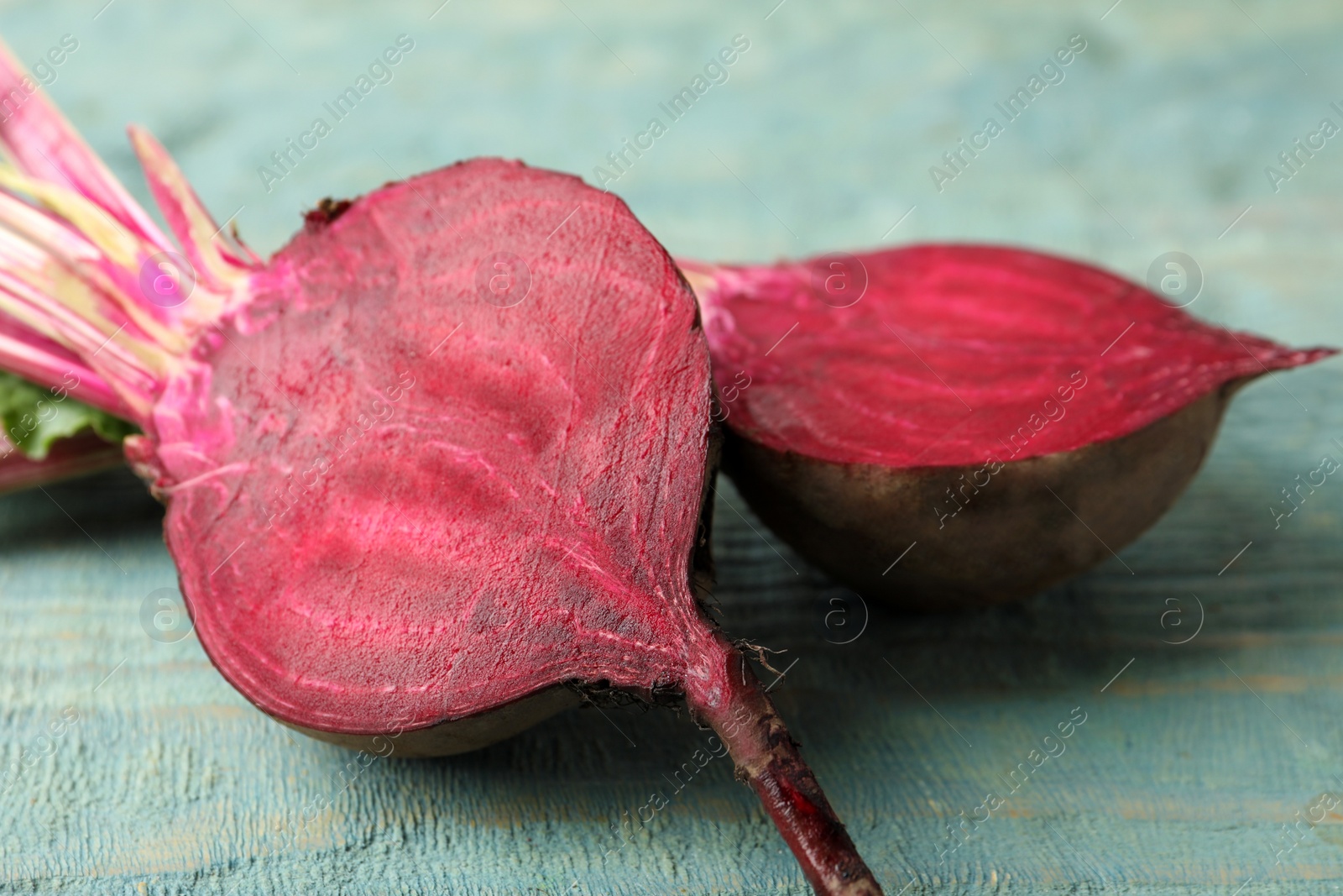 Photo of Halves of raw beet on blue wooden table, closeup