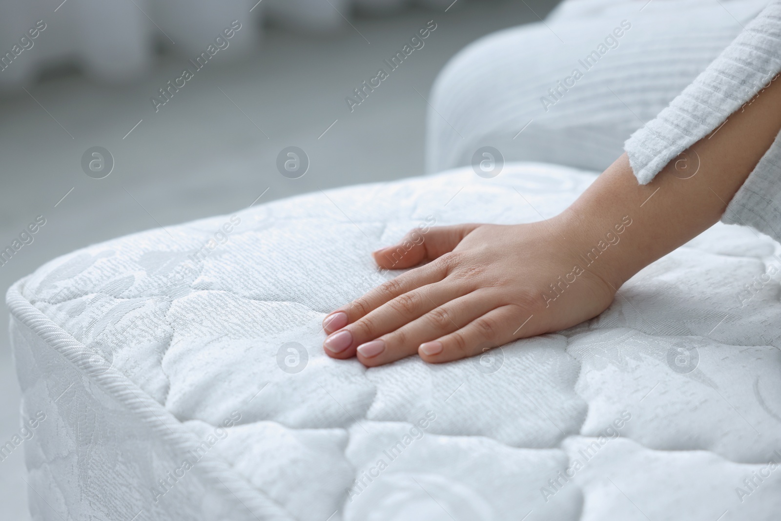 Photo of Woman touching soft white mattress indoors, closeup