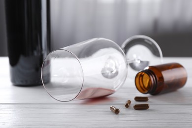 Photo of Alcohol and drug addiction. Overturned glass with red wine, bottle and pills on white wooden table, closeup