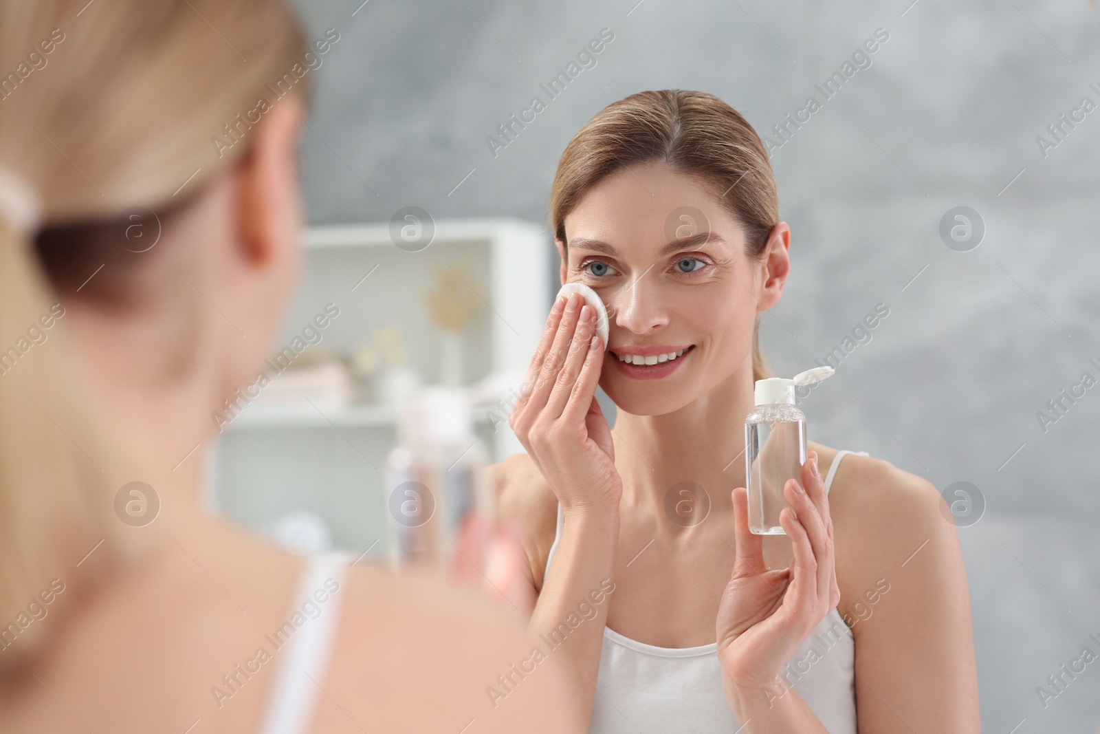 Photo of Beautiful woman removing makeup with cotton pad near mirror indoors