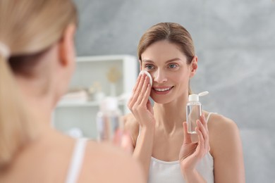 Photo of Beautiful woman removing makeup with cotton pad near mirror indoors