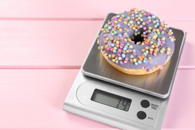 Photo of Kitchen scale with donut on pink wooden table, space for text