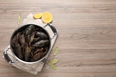 Photo of Fresh raw crayfishes in pot on wooden table, flat lay. Space for text