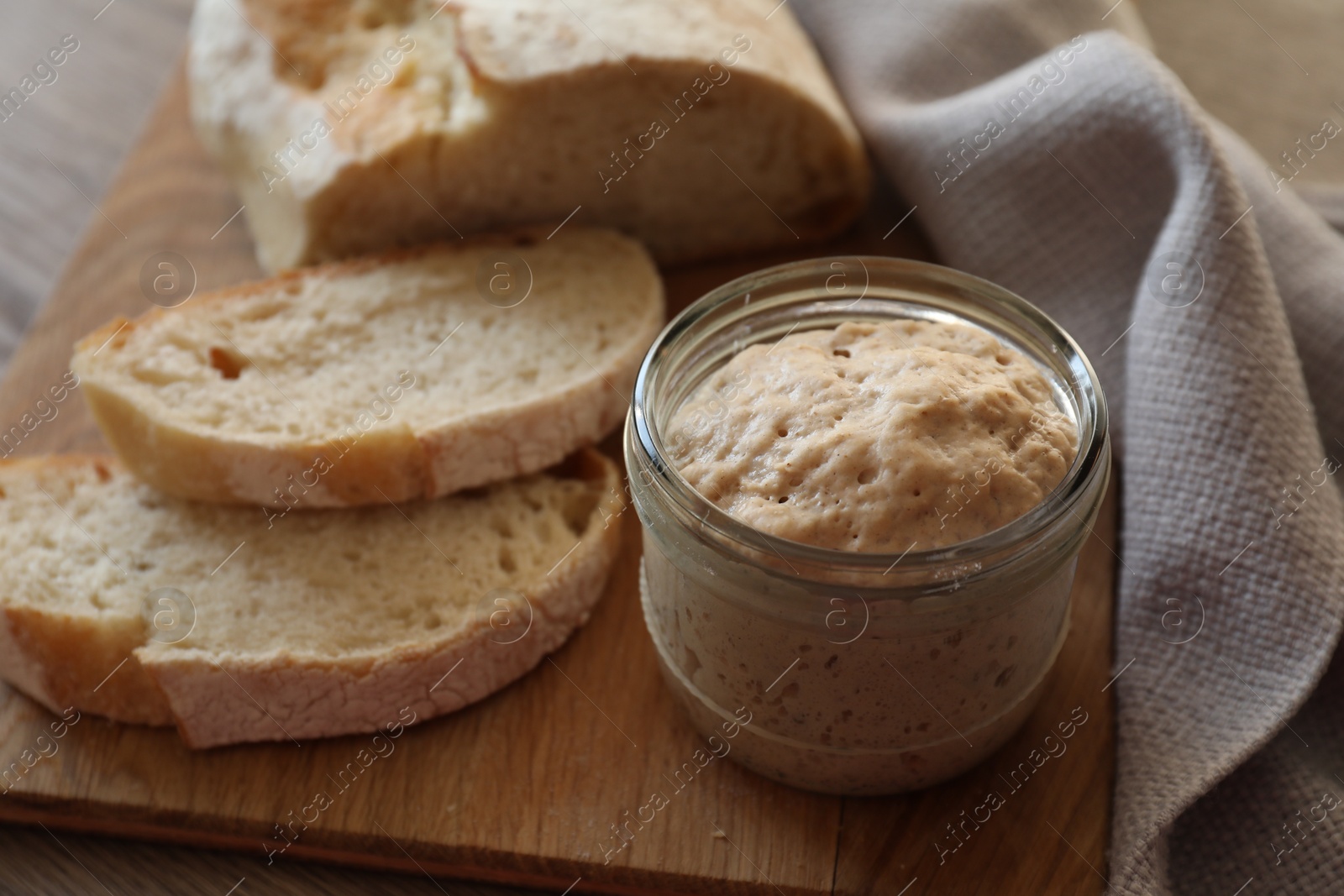 Photo of Sourdough starter in glass jar and bread on table, closeup