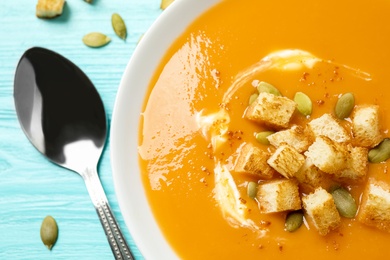 Photo of Tasty creamy pumpkin soup with croutons and seeds in bowl on light blue wooden table, closeup