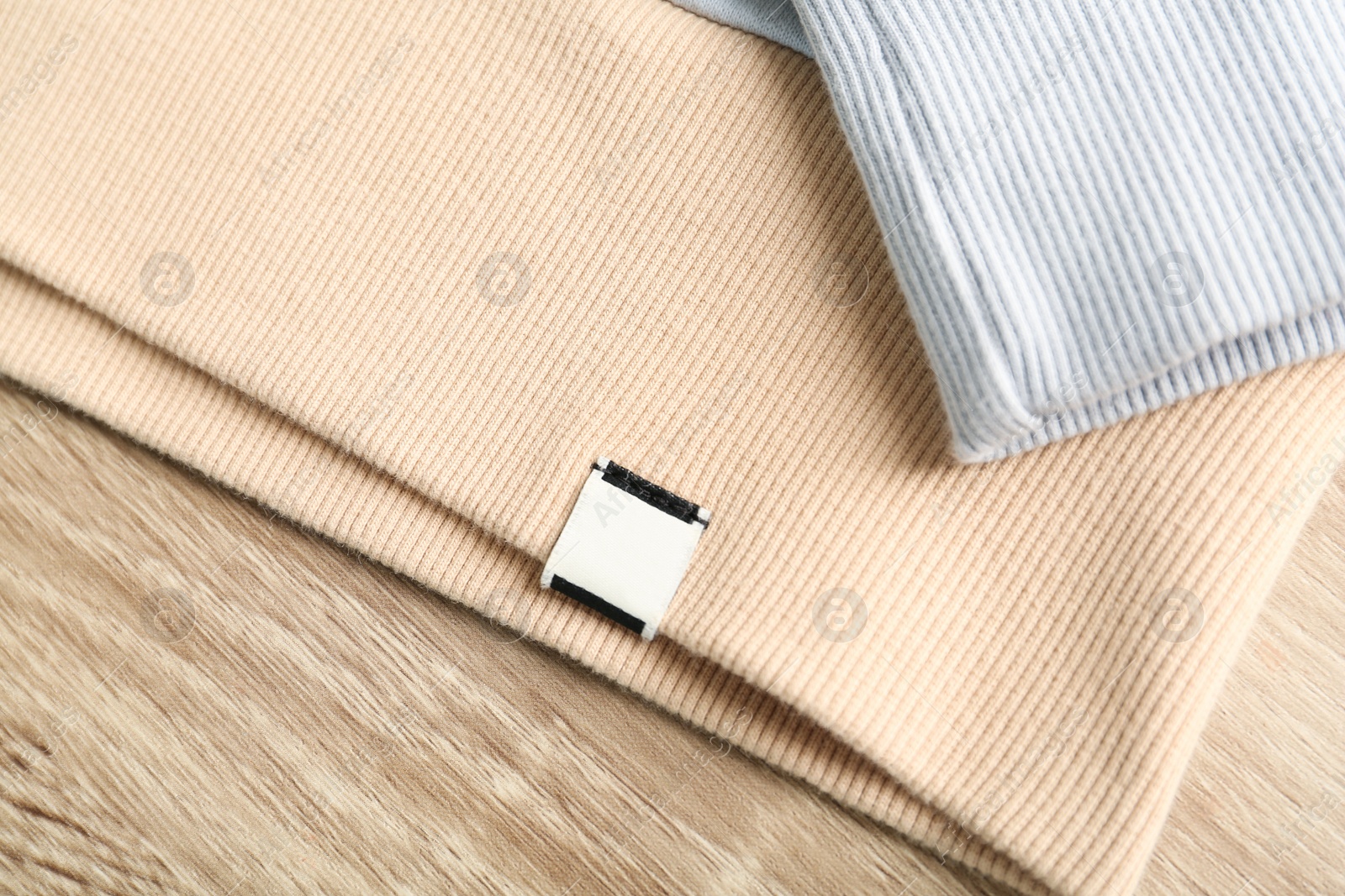 Photo of Beige apparel with blank clothing label on wooden table, top view