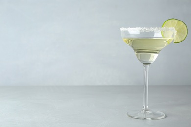 Glass of lemon drop martini cocktail with lime slice on light table against grey background. Space for text