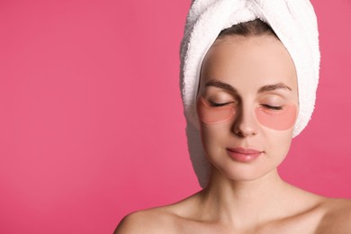 Photo of Beautiful young woman with under eye patches and hair wrapped in towel on pink background, space for text