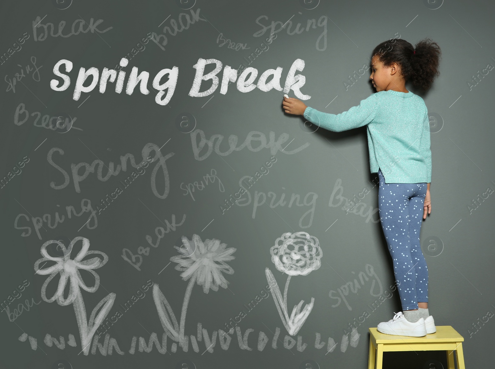 Image of African American girl writing phrase Spring Break with chalk on grey wall. School holiday