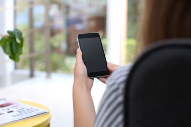 Photo of Woman holding smartphone with blank screen on blurred background. Mockup for design