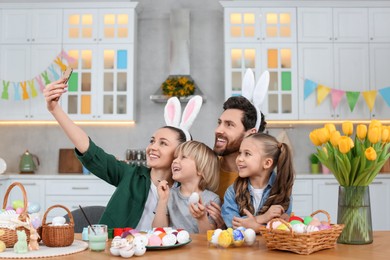 Family making selfie while painting Easter eggs at table in kitchen