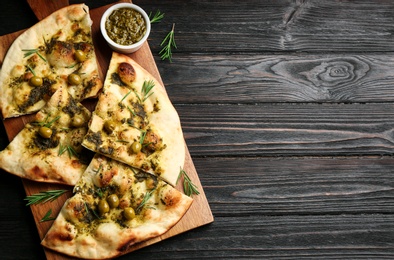 Delicious focaccia bread with green olives on black wooden table, top view. Space for text