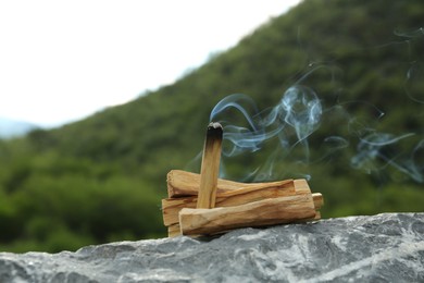 Photo of Burning palo santo stick on stone surface outdoors
