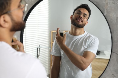 Photo of Man spraying luxury perfume near mirror indoors